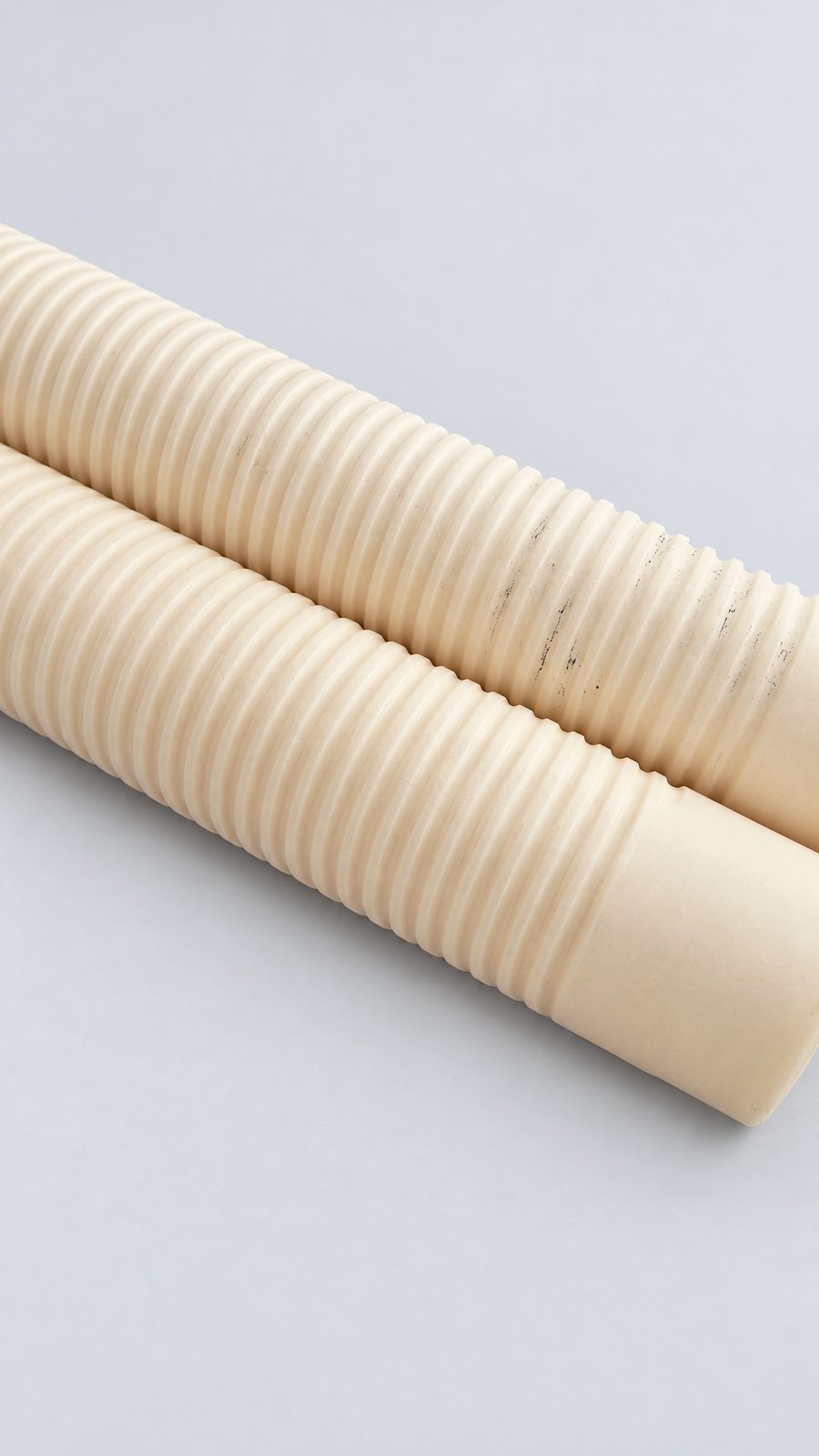 Two cream ceramic tubes on a black surface, each with a continuous helical groove along most of its length and a plain section at one end.