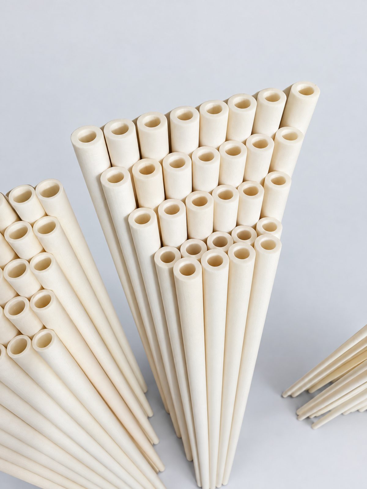 About thirty long, thick-walled ivory tubes with open ends leaning in a fan against a white textured wall.