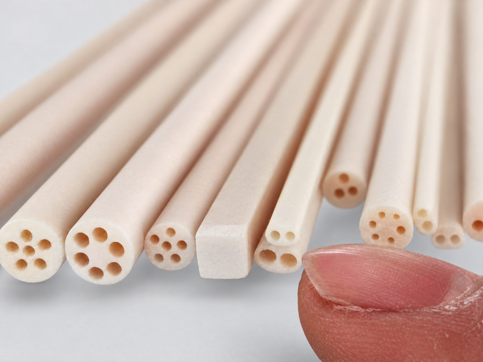 クリーム色の細い絶縁棒の端面の接写：6 穴棒、角棒、2 穴・3 穴・4 穴棒。指先と並べて。