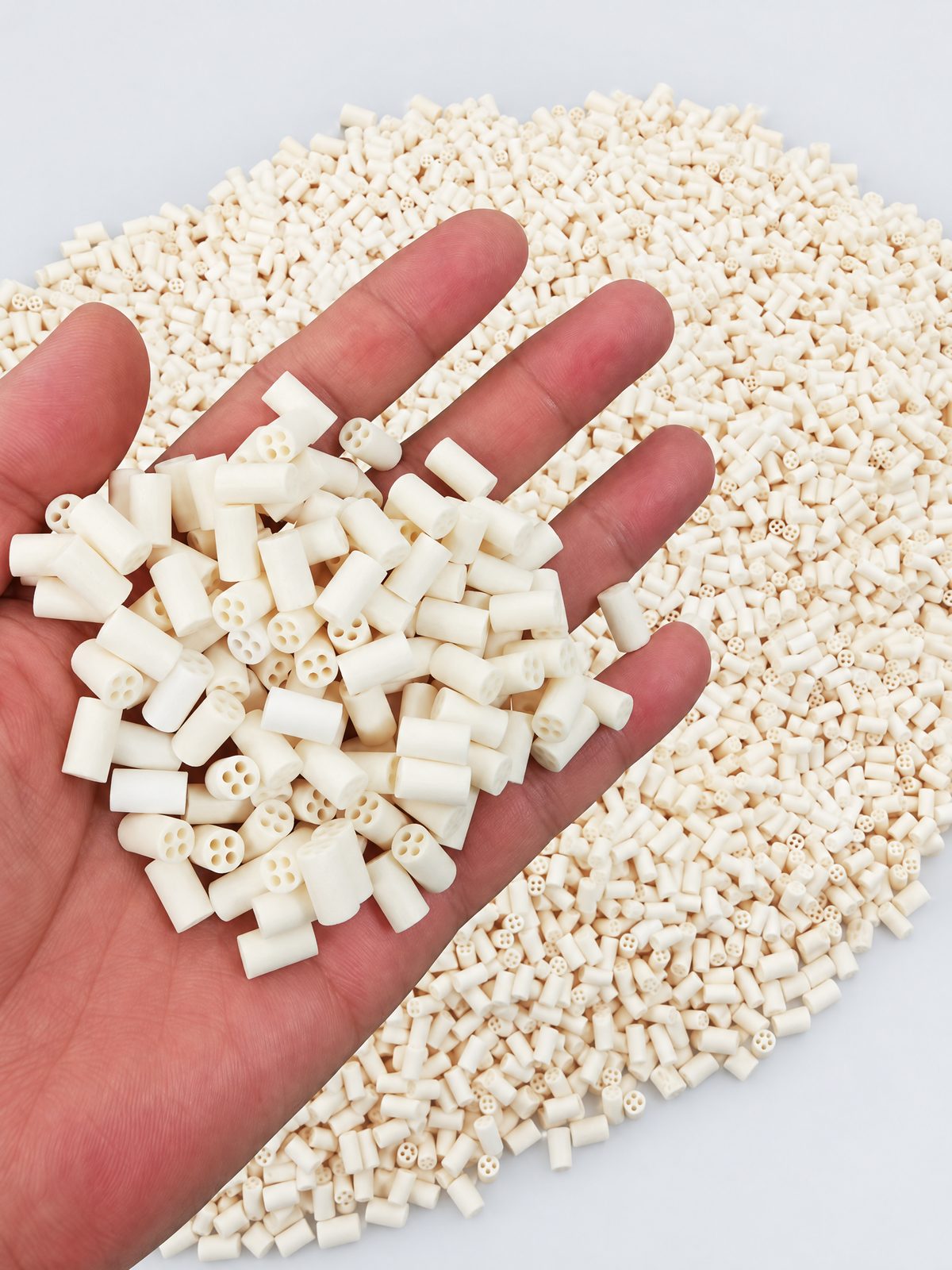 A palmful of short cream four-bore insulator beads held over a blue crate filled with the same beads.