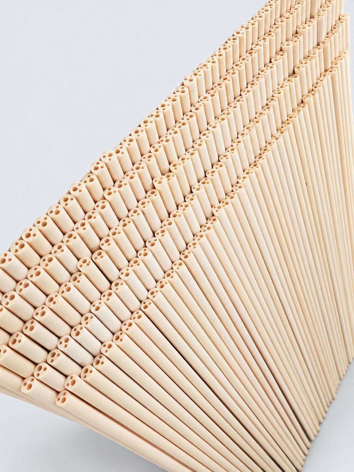 Several hundred cream four-bore insulator rods, two larger and two smaller bores each, standing on end against a white board.
