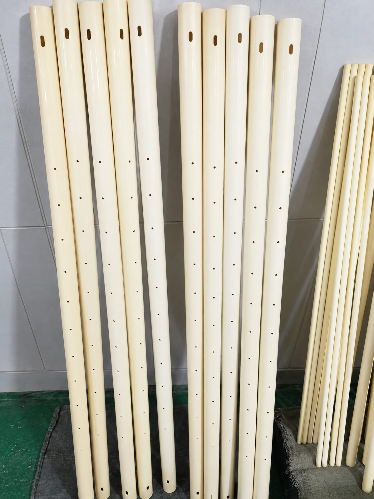 Ivory ceramic tubes leaning against a white tiled wall, each with an oblong slot near the top and a line of small round holes down one side.