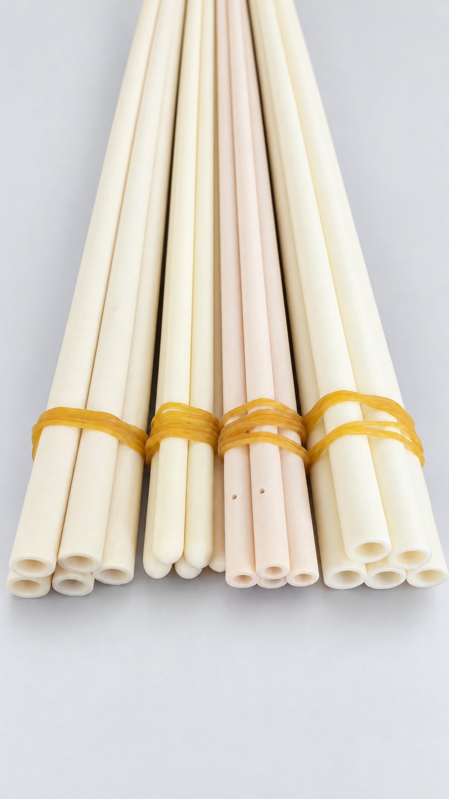 Bundles of long cream-coloured alumina protection tubes with closed ends, tied with yellow bands, on a red cloth.